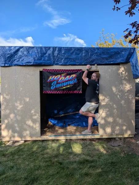 Ty hanging on the door of a homemade shed with a HO DAD Summer banner inside